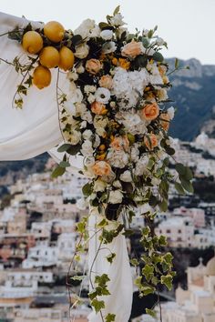 an orange and white floral arrangement on the top of a wedding arch in front of a cityscape