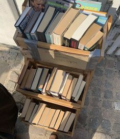 a person standing next to a bookshelf full of books on the sidewalk with their feet propped up