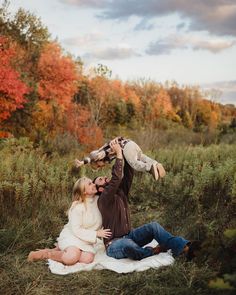 a man and woman are sitting on a blanket while holding their baby in the air