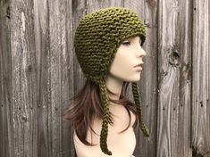 "Knit Hat Style: Garter Earflap Helmet - a chunky knit hat with ear flaps and knitted ties, for women, men and teens. Color: This sample hat is shown in Cilantro, an olive green. Sizes: One size fits average teen or adult head size of 20\" to 23\" (50.5 cm to 58 cm). Fiber Content: 80% acrylic, 20% wool Characteristics: Whimsical, chunky, very soft, warm and cozy. Care Instructions: Hand wash, dry flat. Every item from Pixiebell is handmade and knit or crocheted to order, unless otherwise stated Adjustable Knitted Bonnet For Outdoors, Adjustable Knitted Beanie With Ear Flaps, Warm Beanie With Ear Flaps, Winter Crochet Hat With Ear Flaps, Knitted Beanie With Ear Flaps For Cold Weather, Cold Weather Knitted Beanie With Ear Flaps, Warm Yarn Crochet Hat With Ear Flaps, Knitted Hats With Ear Flaps, Hat With Ear Flaps