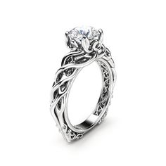 a white gold engagement ring with an intricate design on the band and a round diamond center stone