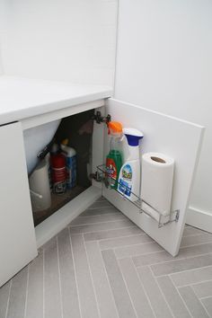 an open cabinet in the corner of a bathroom with toilet paper and cleaning products inside