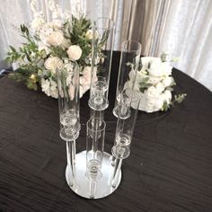 four clear vases sitting on top of a black table next to white flowers and greenery