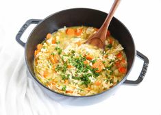 a pot filled with rice and carrots on top of a white table next to a wooden spoon