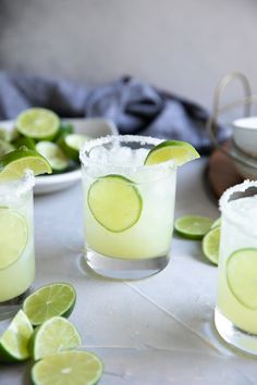 two glasses filled with lime margaritas on top of a table next to sliced limes