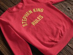 Stephen King Rules Sweatshirt, Monster Squad Inspired Stephen King Rules Sweatshirt, Stephen King Rules Tshirt, Stephen King T Shirt Ideal for any situation, a unisex heavy blend crewneck sweatshirt is pure comfort. These garments are made from polyester and cotton. This combination helps designs come out looking fresh and beautiful. The collar is ribbed knit, so it retains its shape even after washing. There are no itchy side seams on these sweaters.  .: 50% cotton, 50% polyester .: Medium-heavy fabric (8.0 oz/yd² (271.25 g/m .: Loose fit .: Sewn-in label .: Runs true to size Long Sleeve College T-shirt With Branding, Long Sleeve Branded T-shirt For College, Branded Crew Neck Top For College, Fan Apparel Tops With Branding And Crew Neck, Monster Squad, King Tshirt, Stephen King, Sew-in Labels, Unisex Sweatshirt