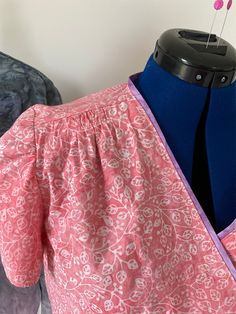 the back of a pink and blue dress with flowers on it, next to a mannequin