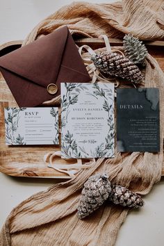 the wedding stationery is laid out on a wooden tray with pine cones and an envelope