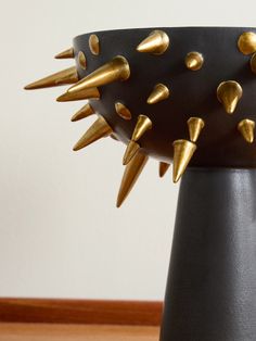 a black and gold vase with spikes on it's sides sitting on a wooden table