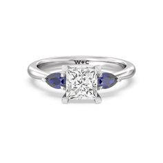 a white gold ring with three blue sapphire stones on the band and a single diamond in the center