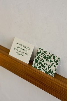 two business cards sitting on top of a wooden shelf next to each other in front of a white wall