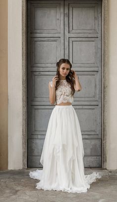 a woman standing in front of an open door wearing a white dress and holding her hair up