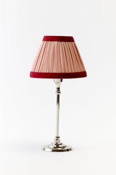 a lamp with a red shade on top of it, against a white wall background