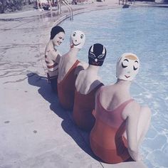 three people in swimsuits sitting on the edge of a swimming pool wearing masks