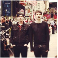 two young men standing next to each other in front of a crowd on a city street