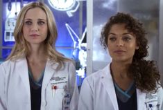 two women in white lab coats standing next to each other and looking at the camera