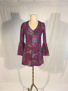 "vintage 1960s long blouse handmade   purple w/pink/green/blue floral print synthetic knit feel- softer, not abrasive or slippery button up front long bell / flounce sleeve open front from waist long enough to be a very mini dress but open flap front would make it best w/leggings or shorts underneath good vintage condition, light wear no size tag, see below measures, lying flat, shoulder-14 1/2\" sleeve-21\" chest-17\" waist-15\" length-31\"     We do not offer returns or refunds unless something is grossly misrepresented. Please contact us within 2 business days of receiving to discuss any possible returns for this reason. We do not offer refunds for your shipping fees. Please feel free to contact us with any questions you may have about an item prior to purchase and we will gladly answer Vintage Purple Top For Spring, Fitted Bell Sleeve Cotton Tops, Fitted Purple Floral Print Top, Fitted Floral Print Blouse With Bell Sleeves, Fitted Printed Purple Tops, Fitted Pink Bohemian Blouse, Vintage Purple Tops With Buttons, Hippie Style Long Sleeve Floral Print Blouse, Fitted Cotton Groovy Tops