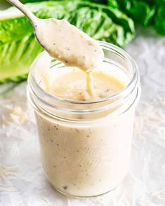 a spoon full of dressing sitting on top of a table next to lettuce