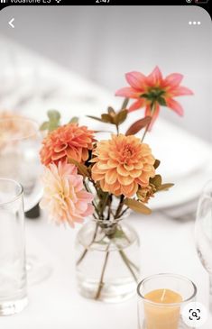 an arrangement of flowers in glass vases on a table with candles and plates behind them