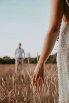 a man and woman standing in the middle of a field with their hands touching each other