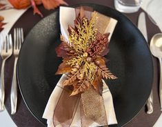 a black plate topped with a napkin covered in fall leaves and gold glittered ribbons