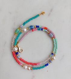 two bracelets with beads and charms on a marble surface, one is multicolored