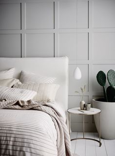 a white bed sitting next to a small table with a potted plant on it