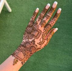 a woman's hand with henna tattoos on it and green grass in the background