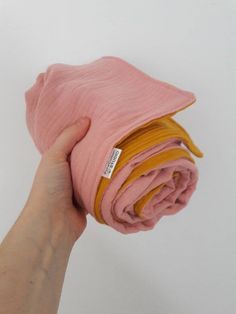 a hand holding a pink and yellow blanket on top of a white surface with the end rolled up