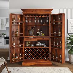 an open wooden cabinet with wine bottles and glasses on the shelves in front of it