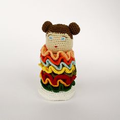 a crocheted stuffed bear sitting on top of a stack of multicolored blankets