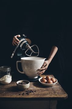 a person mixing ingredients in a bowl on top of a wooden table with an electric mixer