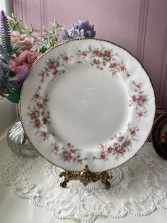 a white plate with pink and purple flowers on it sitting on a table next to a vase