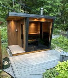 an outdoor sauna in the middle of a wooded area with trees and bushes around it