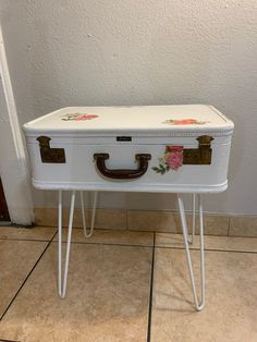 a white suitcase with flowers painted on it sitting on some hairpin legs in front of a wall