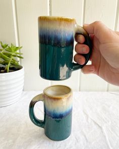 a hand holding a coffee mug next to another cup