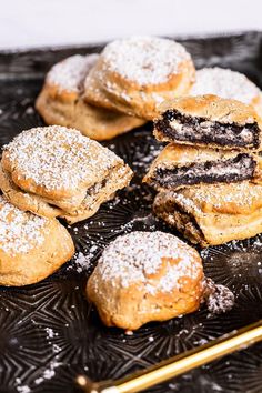 powdered sugar cookies and pastries on a black tray