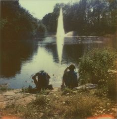 two people sitting on the ground next to a lake