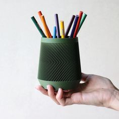 a hand holding a green cup with colored pencils in it and an arrow pattern on the inside