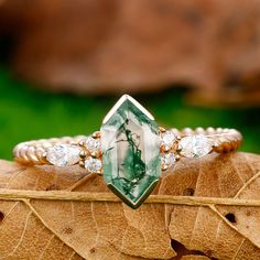 a close up of a ring with a green and white stone in the center on top of a leaf