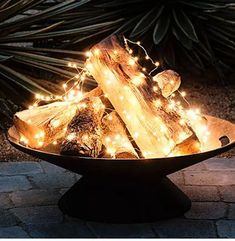 a bowl filled with logs and lights on top of a stone floor next to plants