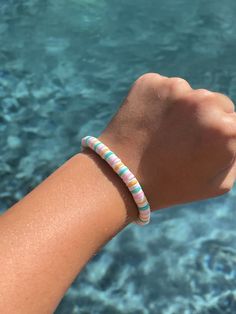 a person's arm with a bracelet on it next to the water and rocks