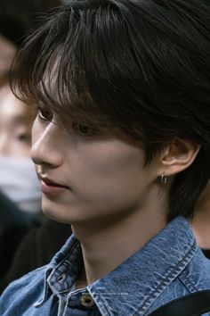 a young man with black hair wearing a denim shirt and looking off to the side