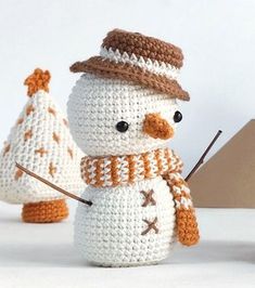 a crocheted snowman holding a knitting needle in front of two knitted christmas trees