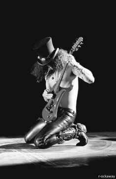 a man with a top hat and boots on sitting down holding a guitar in his lap