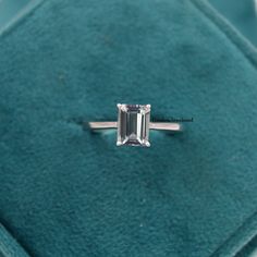 an emerald cut diamond ring sitting on top of a velvet box