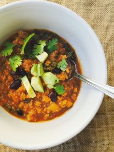 a white bowl filled with chili, avocado and black beans topped with cilantro