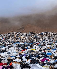 a large pile of clothes sitting on top of a dirt field next to a mountain