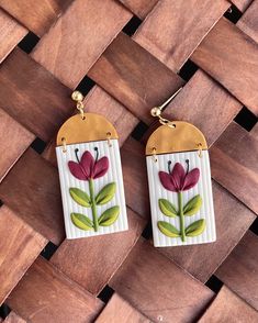 two earrings with flowers painted on them sitting on top of a wooden floor next to each other