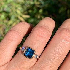 a woman's hand with a blue ring on top of it and three stones in the middle